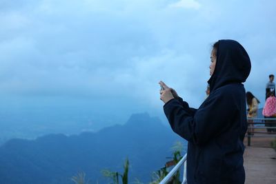 Side view of woman photographing against sky