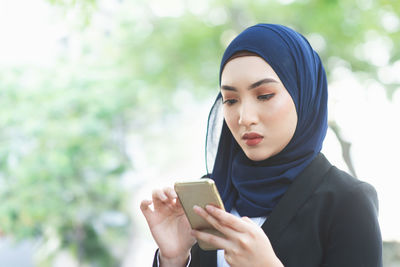 Young woman using mobile phone against trees