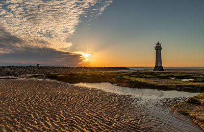 Lighthouse by sea against sky during sunset