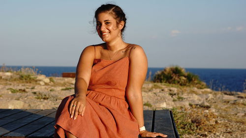 Portrait of smiling young woman standing on beach against sky