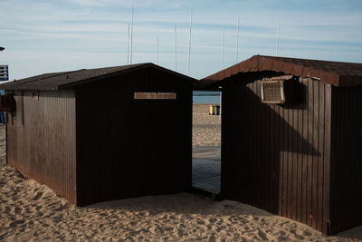 Wooden hut on beach by sea against sky