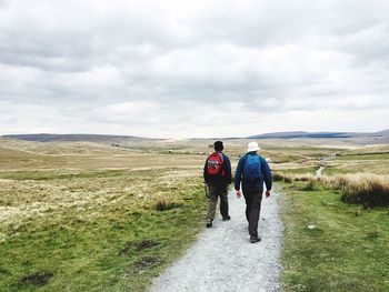 Rear view of people walking on field against sky