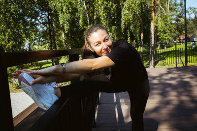 Girl in sportswear on a sunny summer day on the embankment in the park doing fitness and stretching