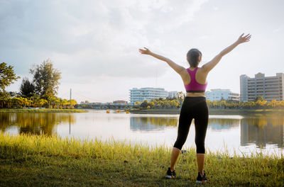 Rear view of woman standing by lake against sky