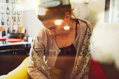 Thoughtful woman sitting on sofa at coffee shop seen though glass