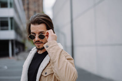 Good looking handsome man looking through sunglasses while posing in urban street with serious face