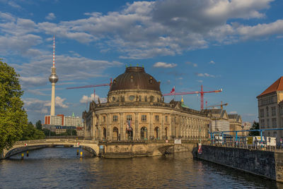 View of buildings by river against cloudy sky