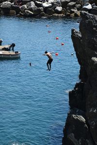 High angle view of men jumping on rock in sea
