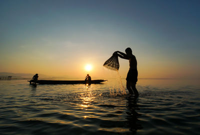 Silhouette people on sea against sky during sunset