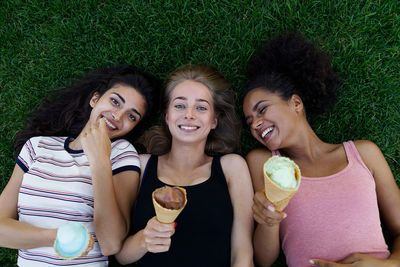 Smiling female friends eating ice cream on field