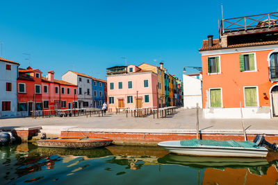 Sailboats moored in canal by buildings against clear blue sky