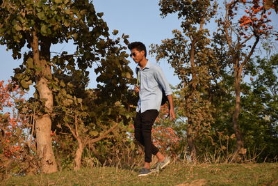 Side view of young man walking on field against trees