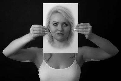 Portrait of young woman standing against black background