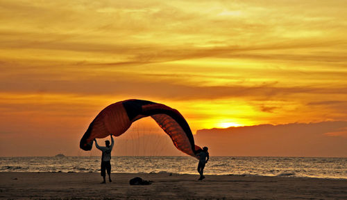 Silhouette people on beach against orange sky