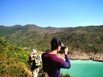 Rear view of man photographing on mountain against clear sky