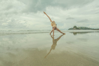 Woman with arms raised on beach against sky