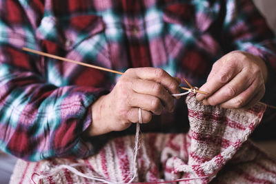 Close up of senior woman hands knitting sweater with needles for grandchild. family bonding and love