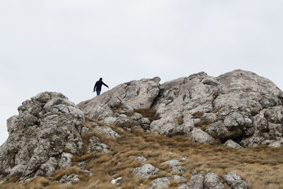 Low angle view of person standing on rock against sky