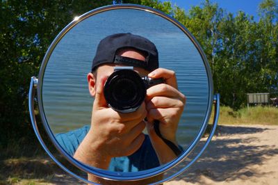 Reflection of man photographing against sea with digital camera seen in mirror