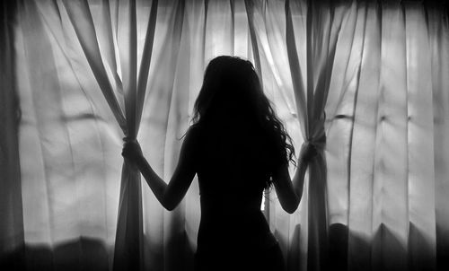 Silhouette of woman standing by curtains at home