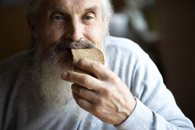 Old sad man with a long gray beard sitting by the table and eating soup and bread