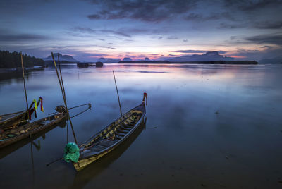 Fishing boats moored in sea against sky during sunset