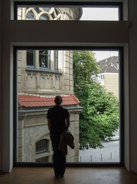 Rear view of man standing by window against building