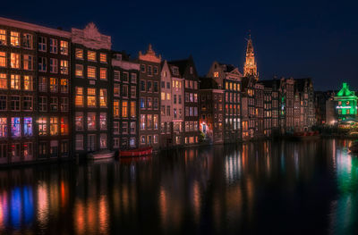 Illuminated buildings by river in city at night