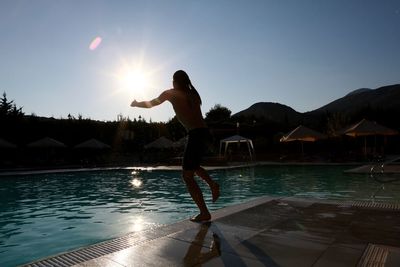 Young man jumping in swimming pool against bright sky