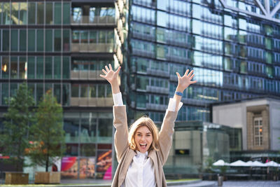 Rear view of woman with arms raised standing in city