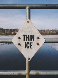 Close-up of thin ice signboard mounted on railing by lake