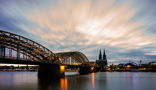 Illuminated bridge over river against cloudy sky