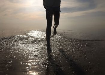 Low section of person at beach against sky during sunset