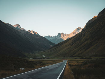 Road leading towards mountains against clear sky