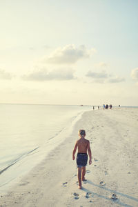 Rear view of shirtless man on beach against sky