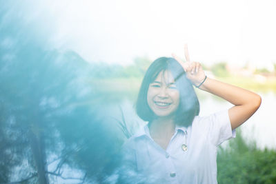 Portrait of smiling woman gesturing peace sign against lake