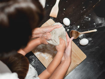 Mother and son are cooking together. mom and toddler knead dough on black table. family time. 