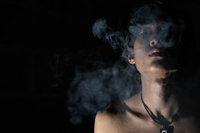 Portrait of man smoking cigarette against black background