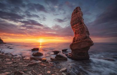 Rock formation on beach against sky during sunset