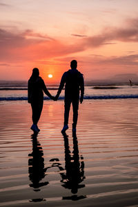 Silhouette people standing on beach against sky during sunset