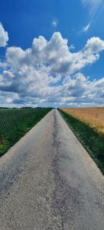 Empty road amidst field against sky