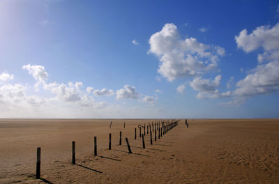 Wooden posts on sand against sky