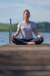 Woman meditating on dock at the lake outdoors in summer