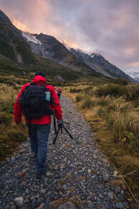 Rear view of men walking on field towards mountain against cloudy sky