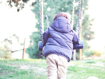 Rear view of boy leaning on swing at park