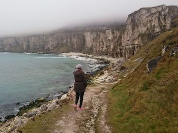 Full length of woman standing on cliff by sea