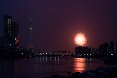 Reflection of firework display on river against sky