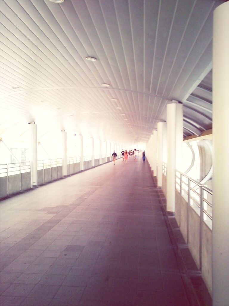 the way forward, indoors, diminishing perspective, architecture, built structure, transportation, vanishing point, ceiling, incidental people, in a row, empty, connection, walking, long, architectural column, lighting equipment, day, railing, corridor