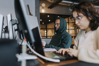 Young male computer programmer working by female colleague at desk in creative office