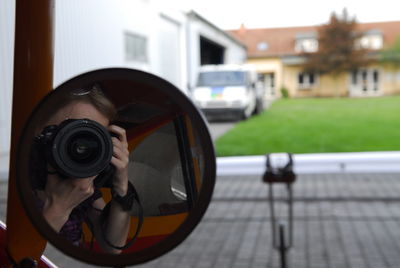 Close-up of woman photographing self in side-view mirror